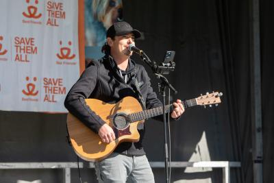 Person holding a guitar and singing on stage at Strut Your Mutt