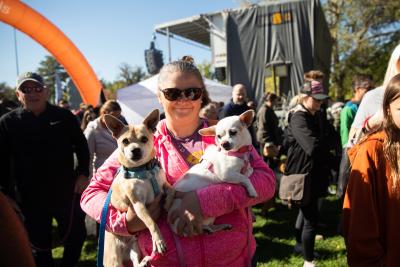 Person holding two small dogs in front of the orange arch at Strut Your Mutt