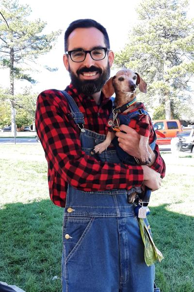 Person and dog he's holding dressed up matching in red flannels and blue overalls