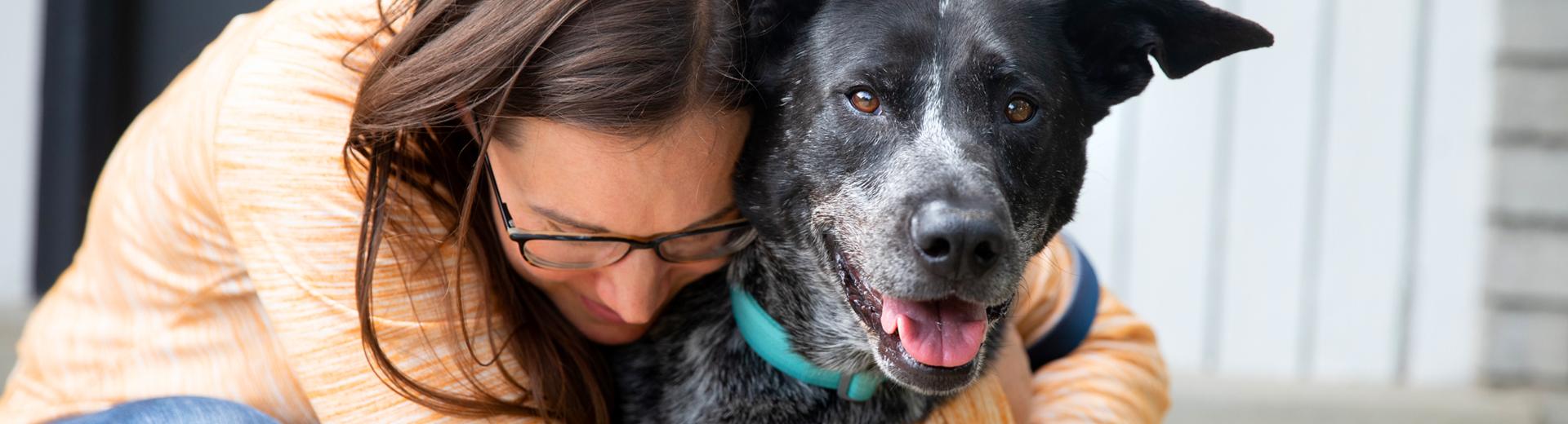 Smiling person hugging on a dog while sitting on steps leading into a home