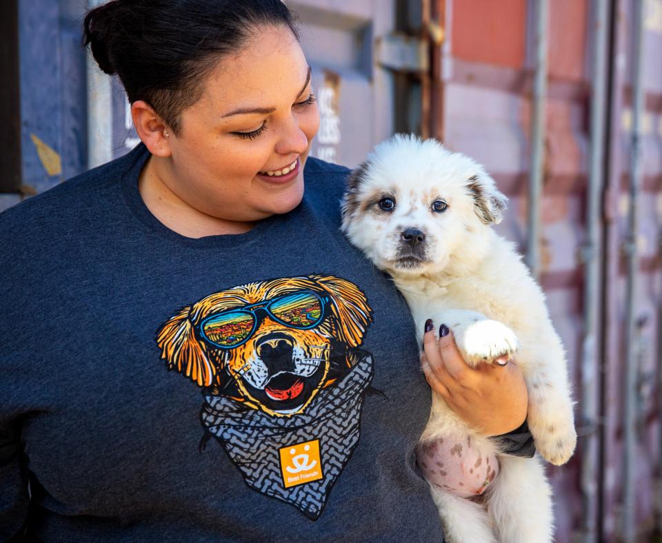 Smiling person wearing a Best Friends sweatshirt looking down at a puppy she's holding