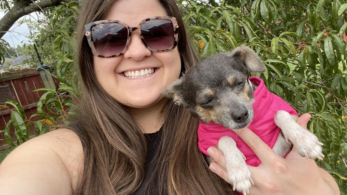 Selfie of Katie holding Berry the dog, who is wearing a pink jacket