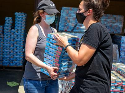 Pair of masked people carrying cases of pet food