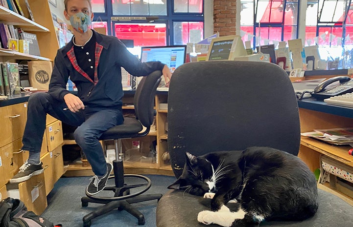 Adam Lipman sitting behind Malcolm the cat, asleep on a chair