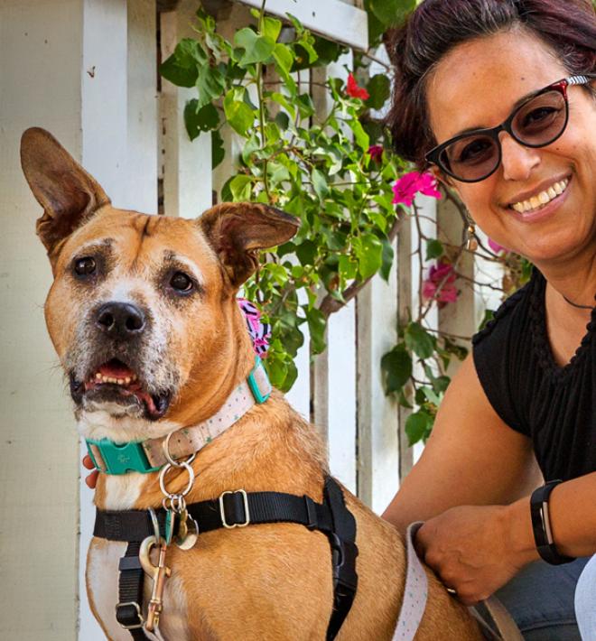 Smiling person kneeling down next to a dog on the sidewalk