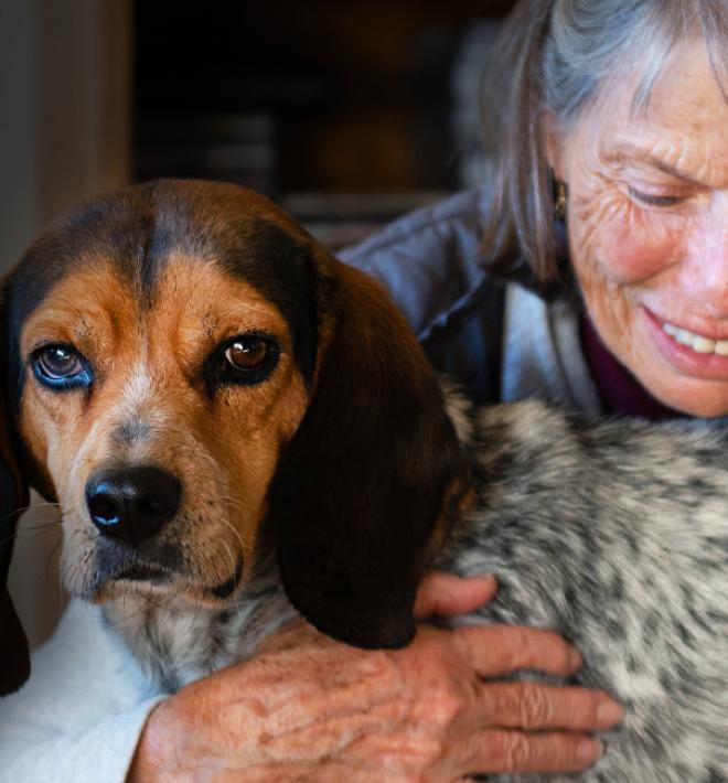 Smiling person kneeling down to hug a dog