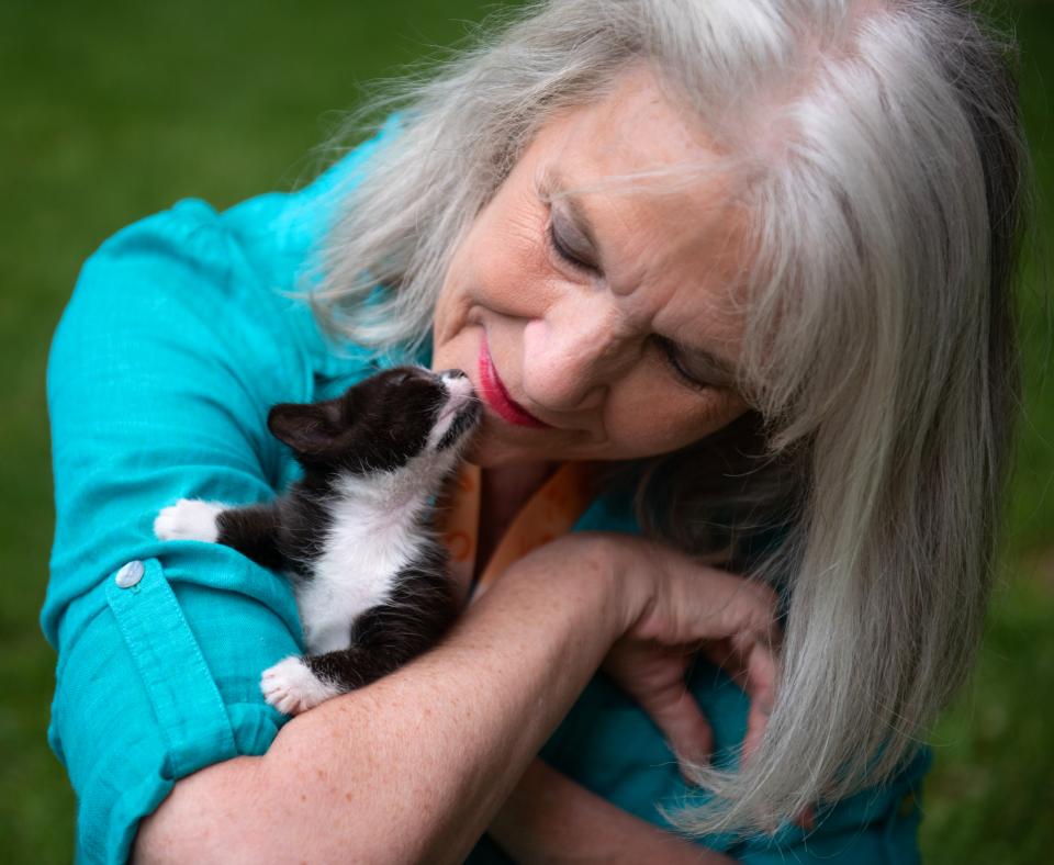 Smiling person holding a tiny kitten close to them in their arms