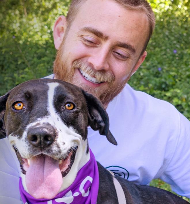 Smiling person kneeling in grass holding a happy dog in their arms