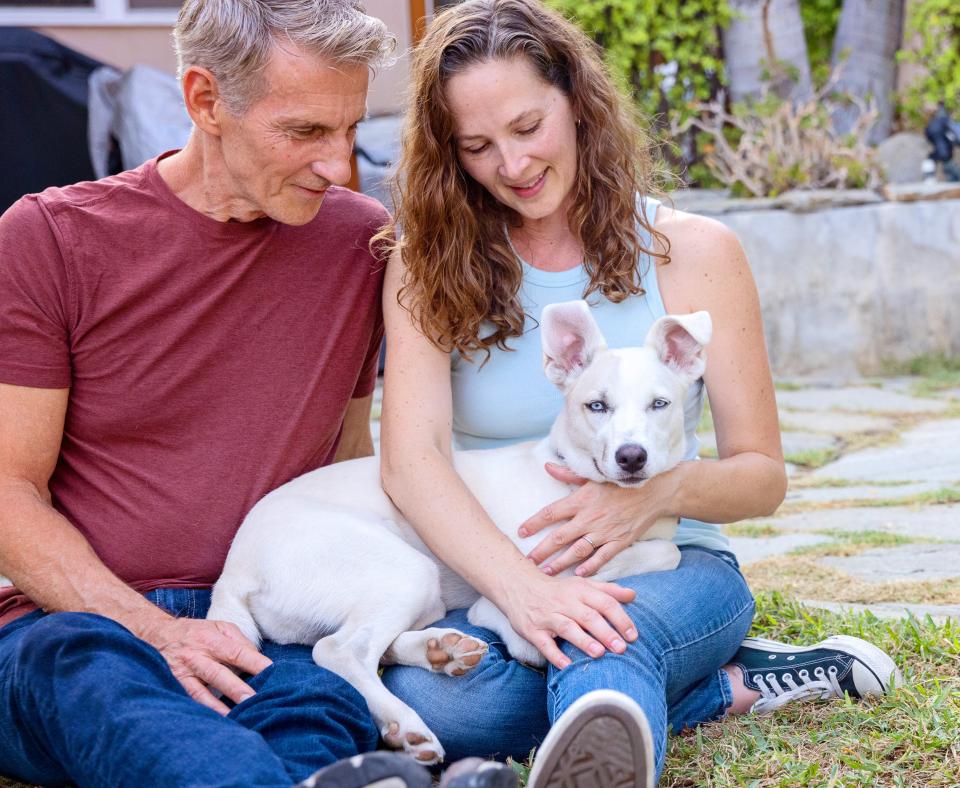 Two smiling people sitting on grass with their dog