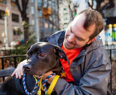 Smiling volunteer sitting with a dog on a bench in New York City