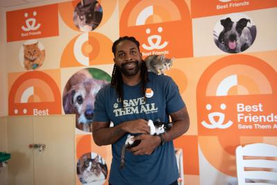 Abdul smiling while holding one kitten with another kitten on his shoulder, wearing a Save Them All T-shirt