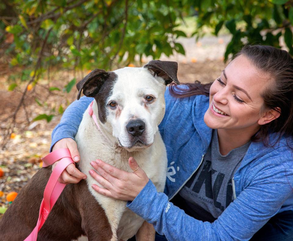 Smiling person kneeling down next to a dog outside