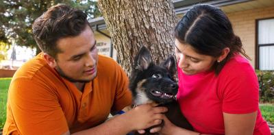 Two smiling people outside in a yard with a puppy