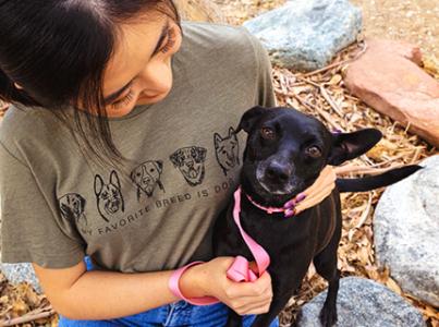 Person looking down at and hugging a small black dog