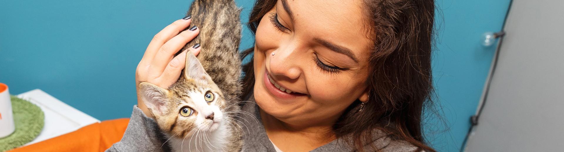 Smiling person petting a tiny kitten on their shoulder