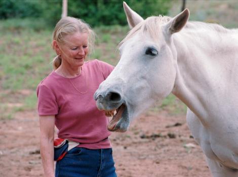 Best Friends Animal Society co-founder Diana Asher outside with a white horse whose mouth is open