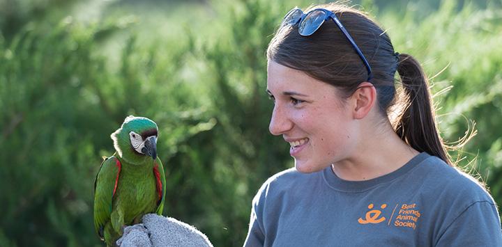 Young woman wearing a Best Friends shirt holding a small parrot on a towel on her hand