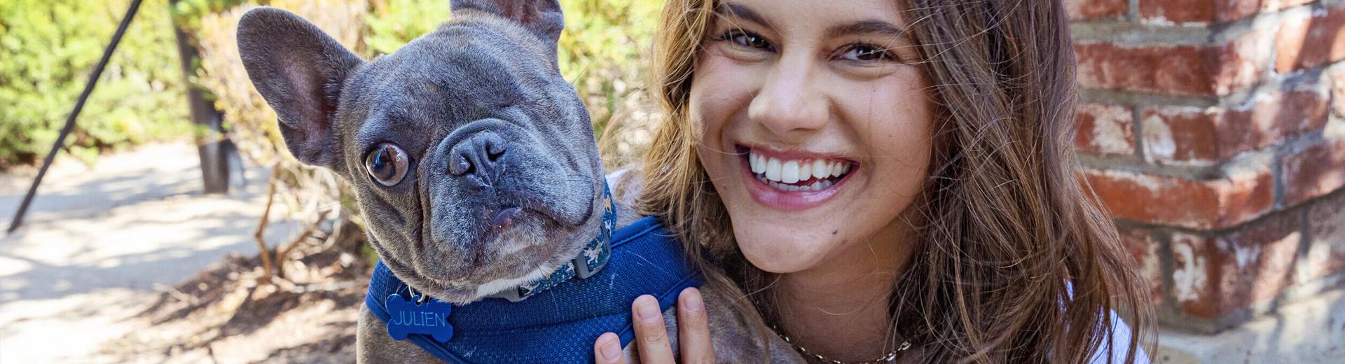 Smiling person holding a small French bulldog with one eye