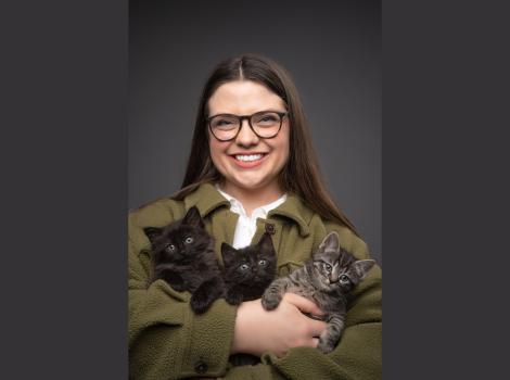 Smiling person holding three kittens in her arms