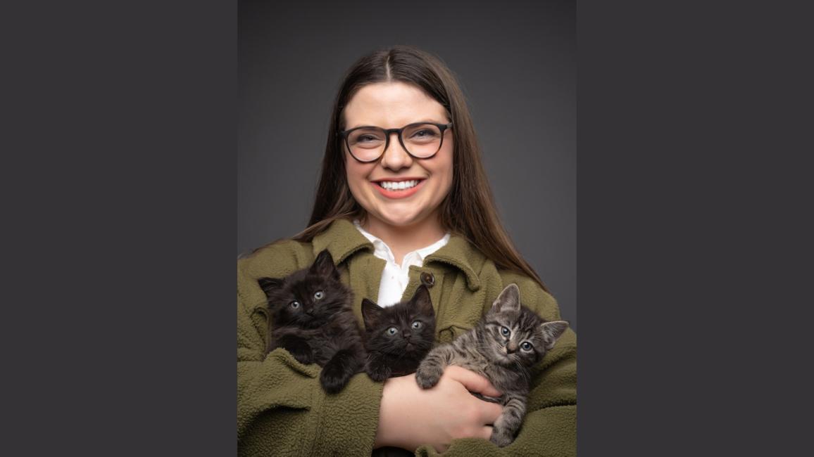 Smiling person holding three kittens in her arms