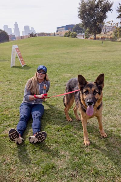 Person sitting in the grass with a German shepherd dog on a leash