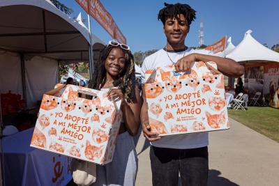 Two people holding cardboard carriers containing cats, with writing on the outside of the carriers in Spanish