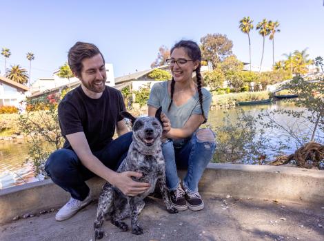 Two people sitting outside with a happy dog between them