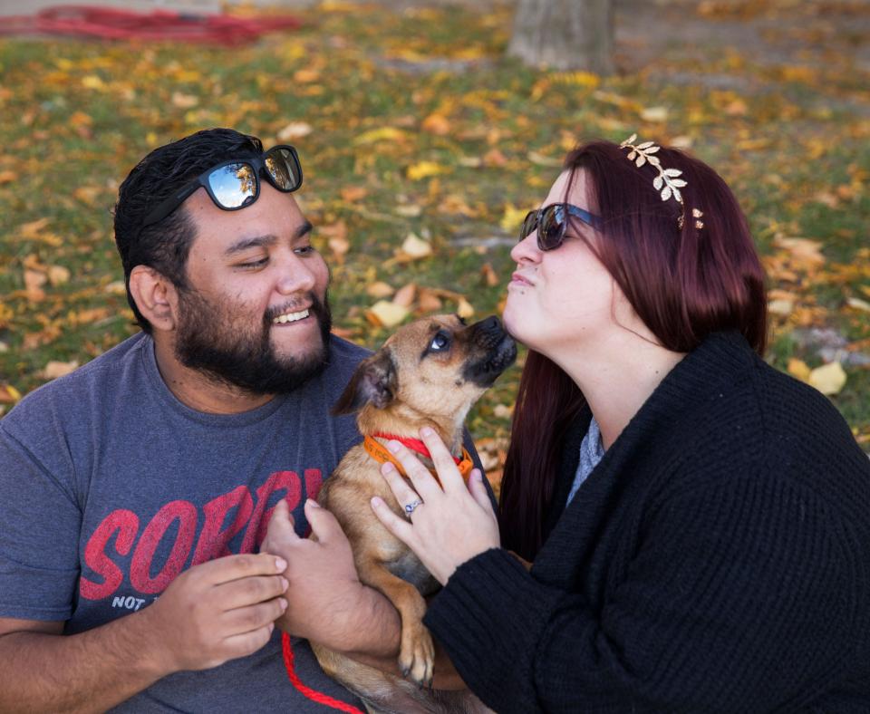 Smiling couple outside on the grass with a small dog between them