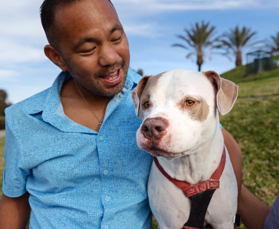 Person smiling at a dog they're sitting next to on the grass