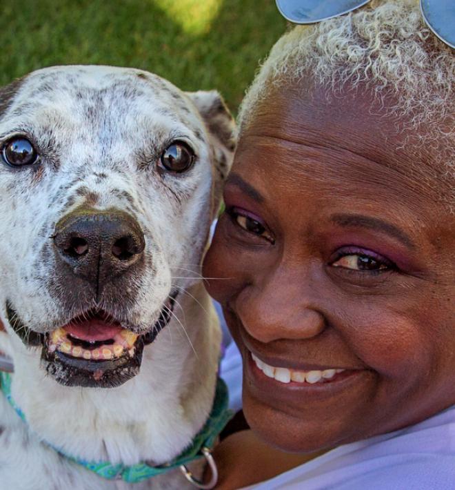 Smiling person holding their dog close while relaxing on a patio