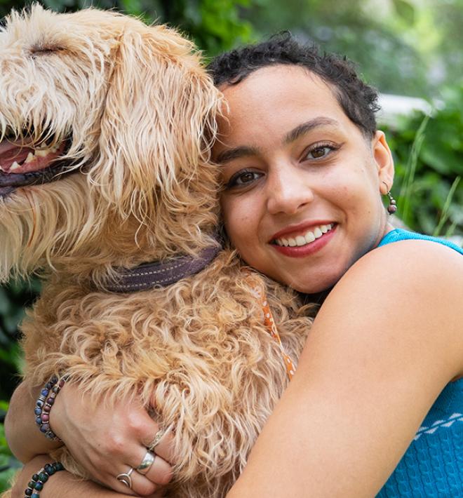 Person hugging a large, tan dog, outside on a lawn