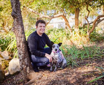 Person sitting outside with a dog under some trees