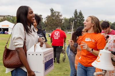 Person holding a cat carrier with her cat talking to a person wearing a Best Friends orange volunteer T-shirt at the Los Angles Super Adoption