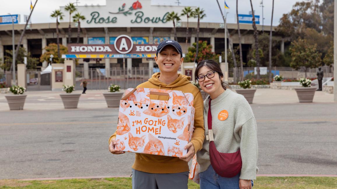 Couple holding a cat carrier containing the cat they adopted in front of the Rose Bowl