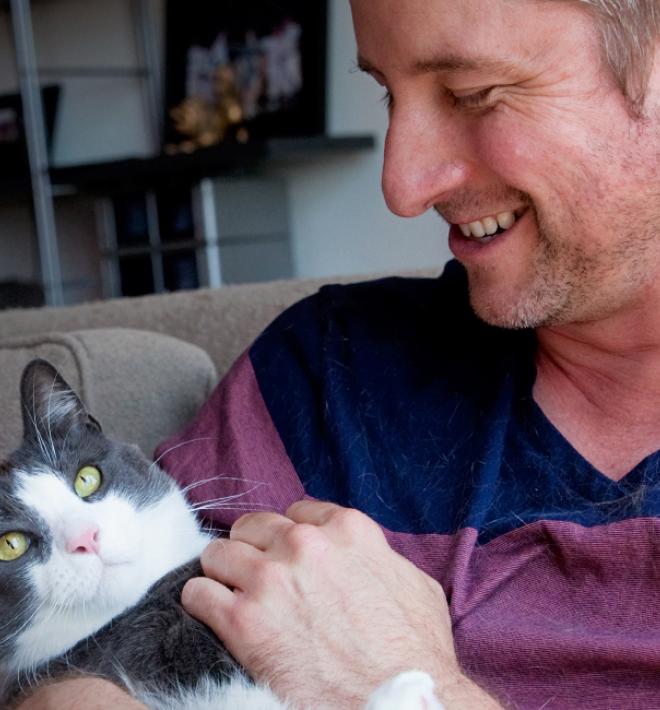 Smiling person relaxing on a couch while holding a cat