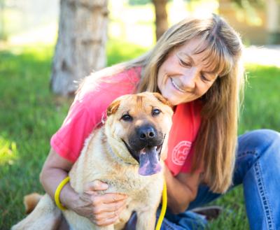 Smiling person sitting in the grass next to a happy dog