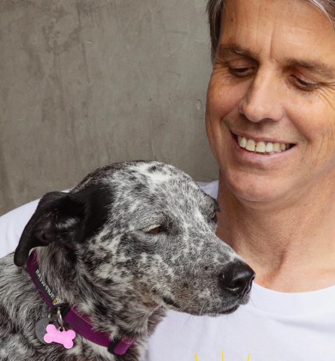 Smiling person sitting outside against a cement wall with a dog