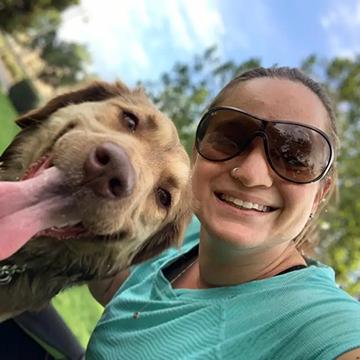 Tilted photo of Yael with a smiling dog whose tongue is out