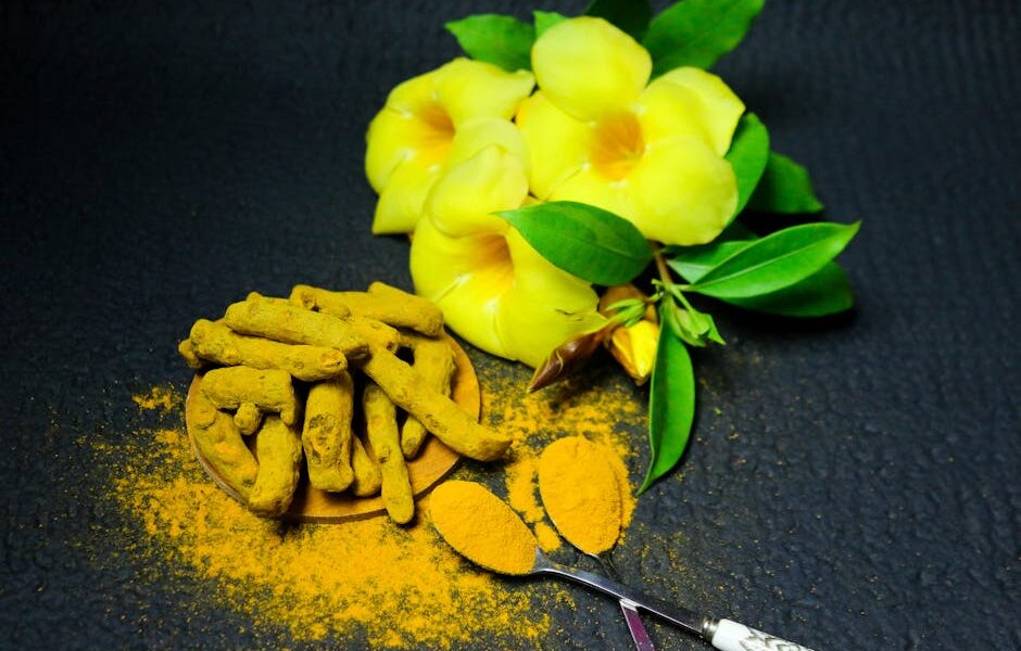 A vibrant display of turmeric root, powder, and yellow flowers on a textured black background.