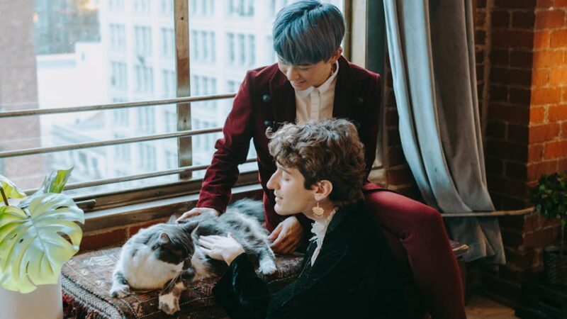 A couple shares a cozy moment with their cat by a large window in an urban apartment.