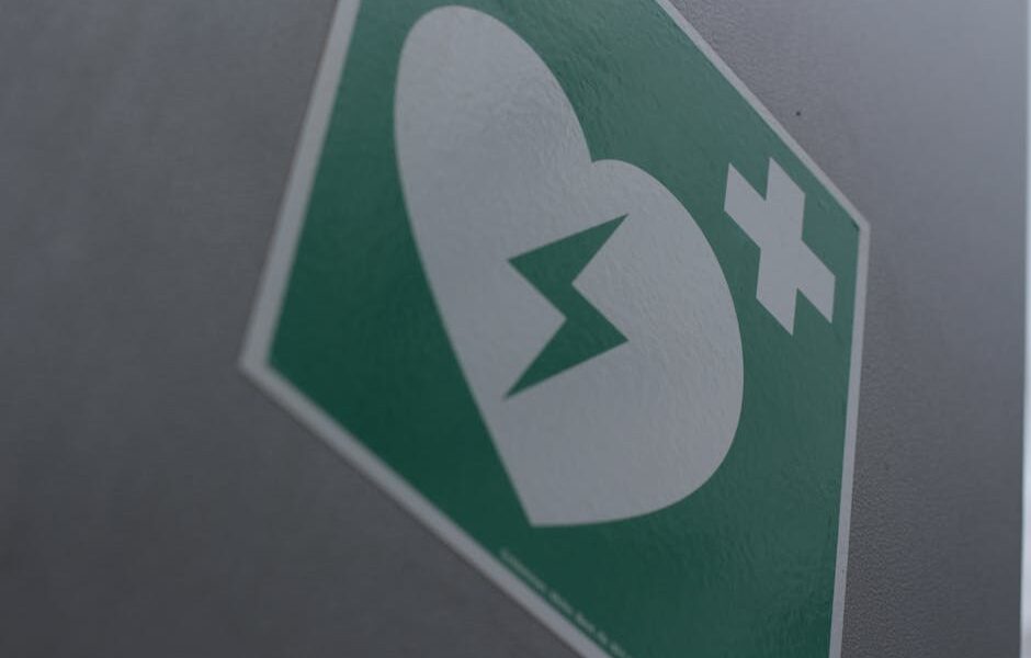 Green first aid sign featuring a broken heart and cross symbol for medical emergency awareness.