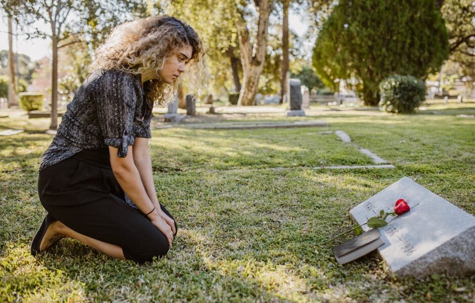 A woman kneeling by a grave in a sunlit cemetery, expressing grief and remembrance.