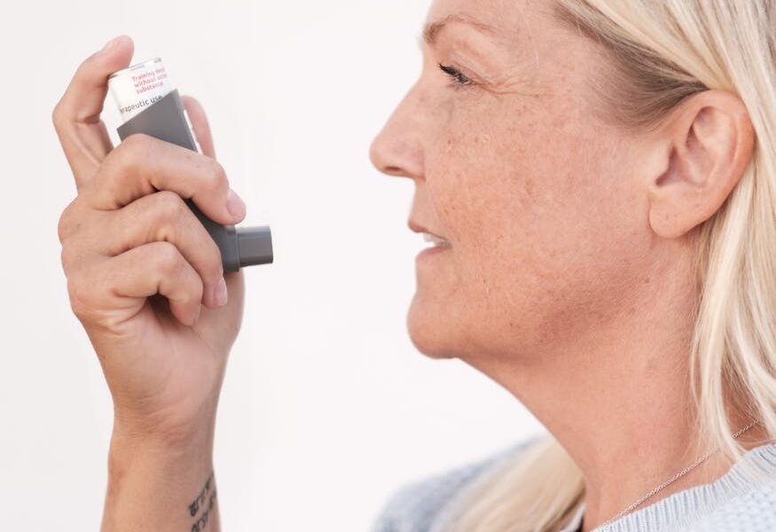 Middle-aged woman using an asthma inhaler to alleviate breathing difficulties.