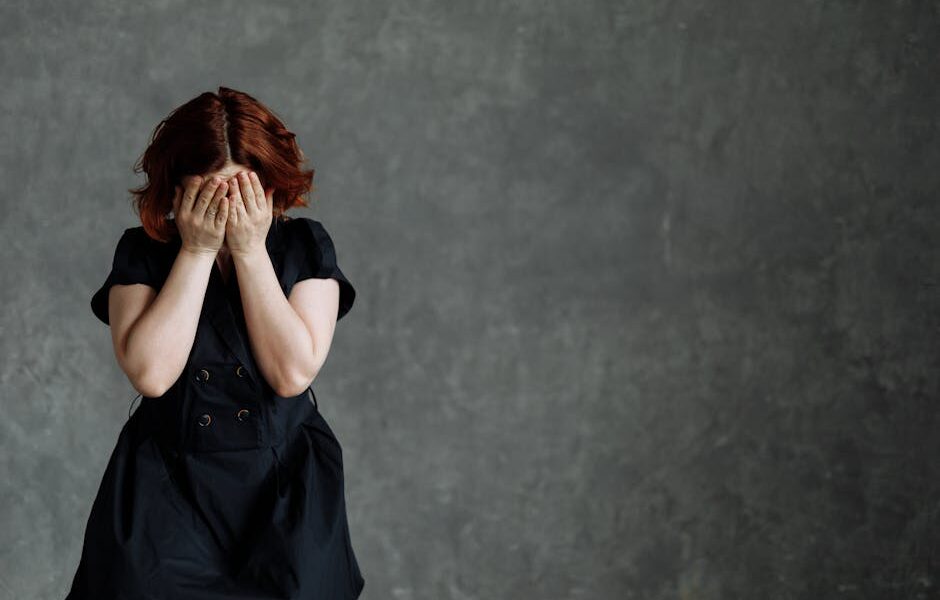 A woman in a black dress expressing emotion against a concrete backdrop, highlighting themes of sadness and stress.