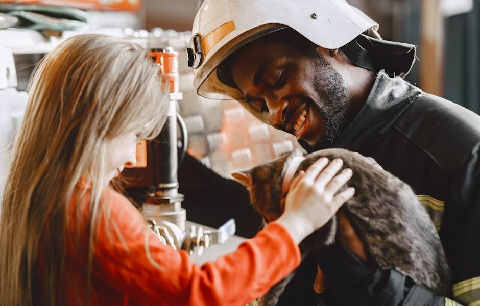 Smiling firefighter and child petting a cat indoors, creating a warm and joyful scene.