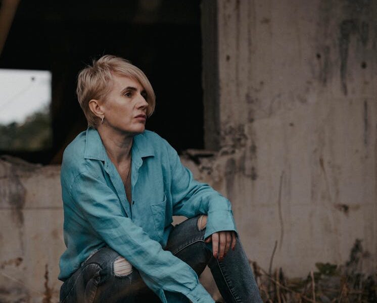 Woman in denim and blue shirt sits near an old building, exuding style and contemplation.