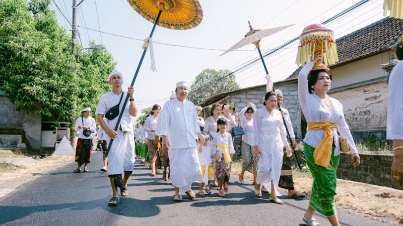 A Balinese procession with traditional attire and vibrant umbrellas on a sunny day.